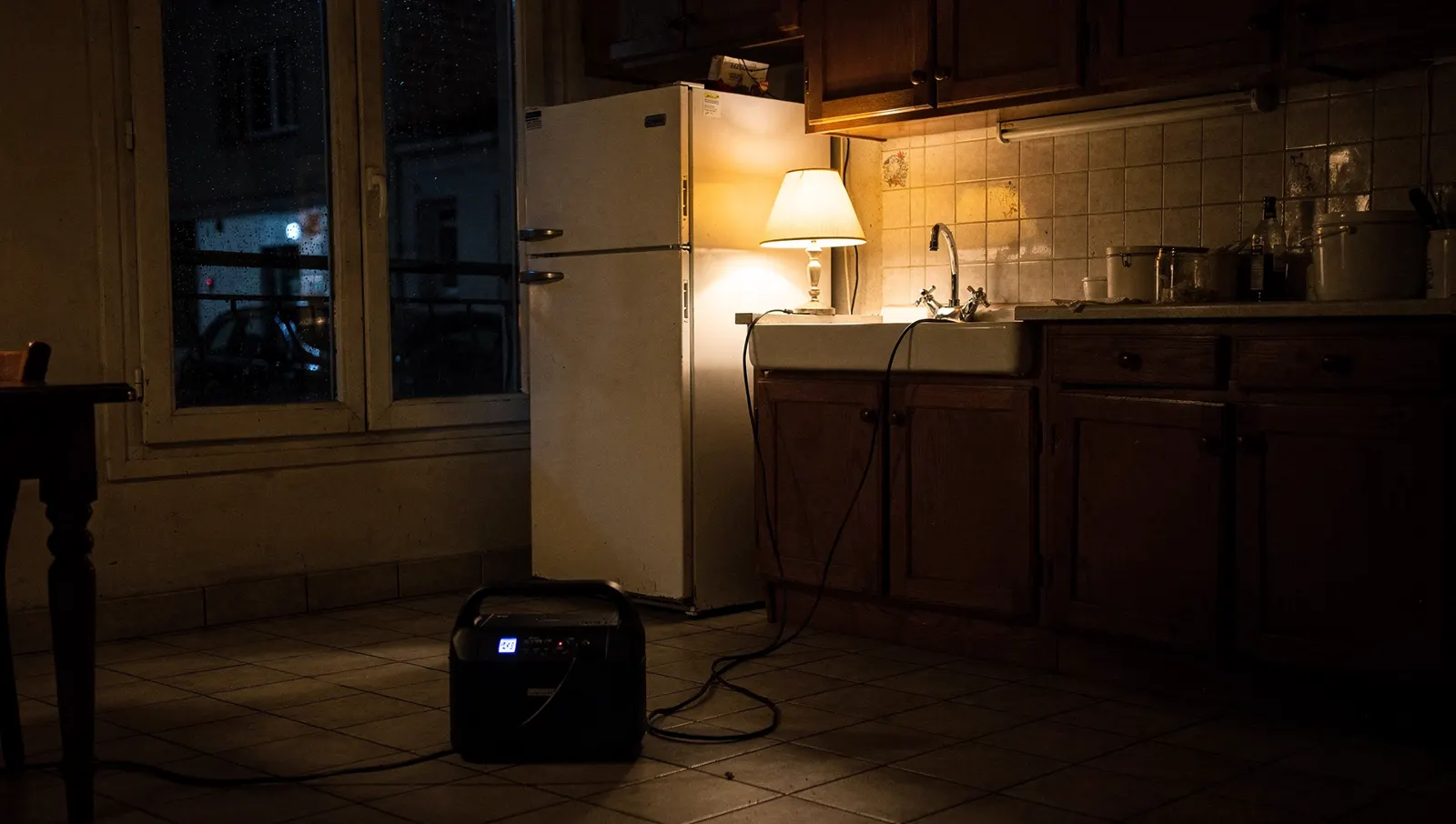 Cuisine plongée dans le noir pendant une coupure de courant, une station électrique alimente le réfrigérateur et une lampe